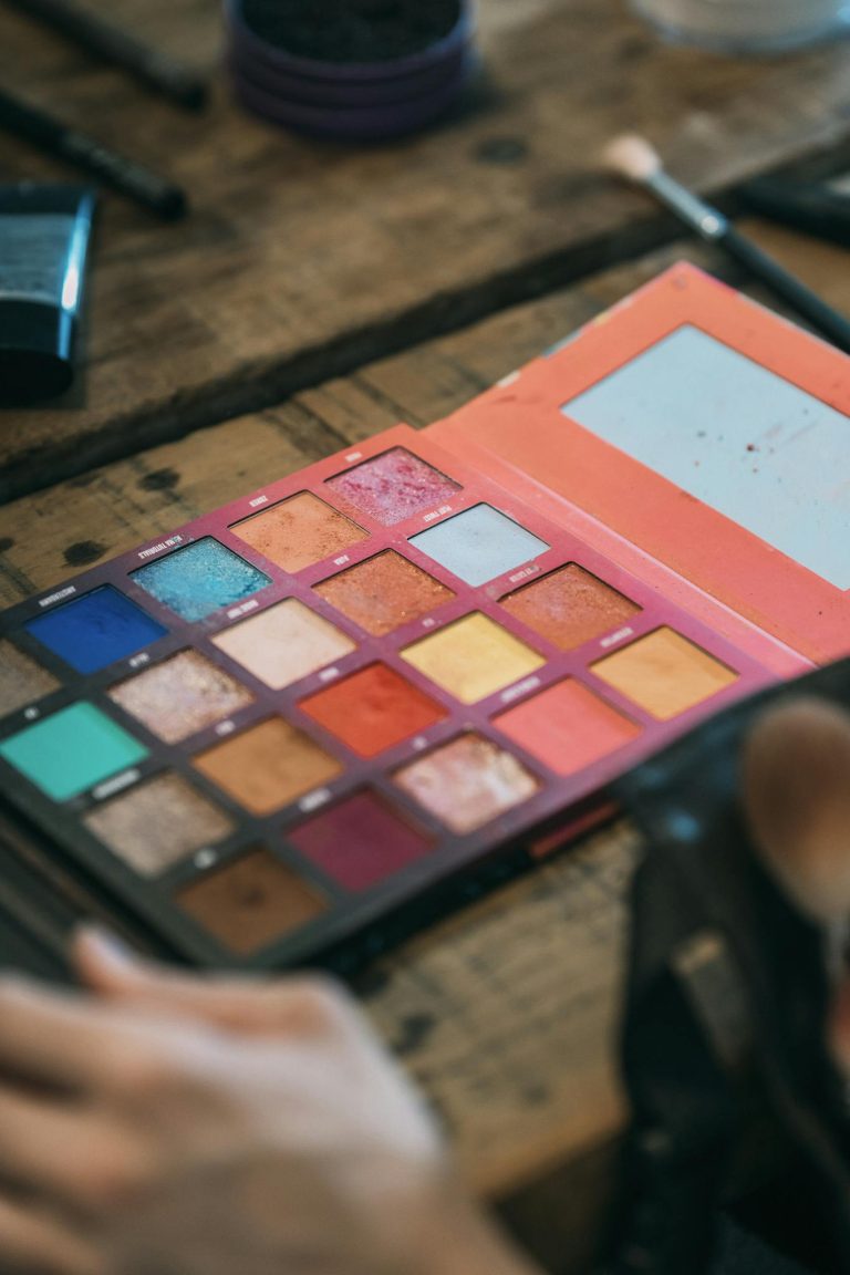 From above kit of eyeshadows of different color in box lying on wooden table near cosmetic brush